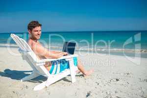 Man using laptop on deck chair at the beach