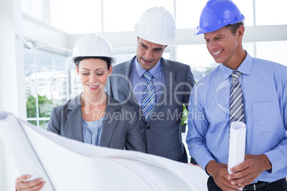 Businessmen and a woman with hard hats and holding blueprint