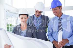 Businessmen and a woman with hard hats and holding blueprint