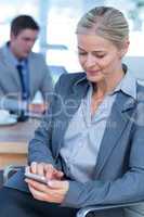 Businesswoman texting on her mobile phone with colleague in back