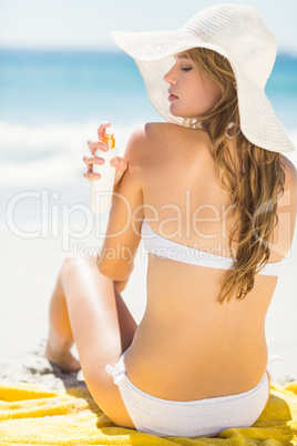 Pretty blonde woman putting sun tan lotion on her shoulder