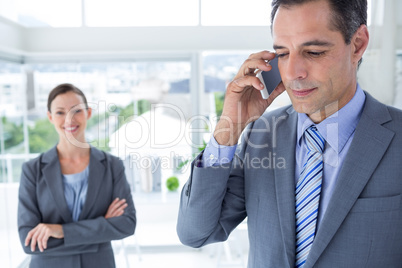 businessman using his phone while his colleague is smiling at th