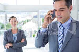 businessman using his phone while his colleague is smiling at th