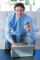 Smiling businessman using laptop and mobile phone on couch