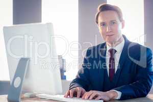 Smiling businessman typing on laptop and looking at camera