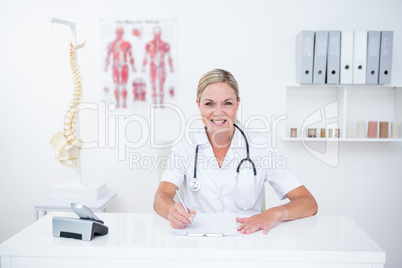 Smiling doctor writing on clipboard at her desk