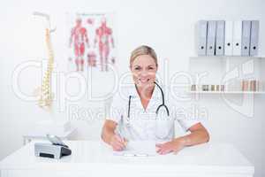 Smiling doctor writing on clipboard at her desk