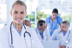 Smiling female doctor looking at camera while her colleagues wor