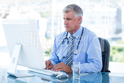 Serious doctor working on computer at his desk