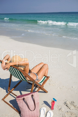 Rear view of pretty brunette relaxing on deck chair at the beach