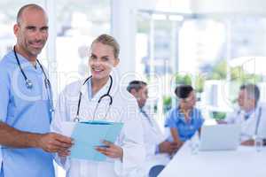 Two doctors holding clipboard while their colleagues working