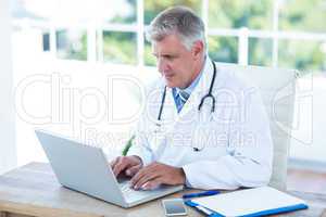 Serious doctor working on laptop at his desk