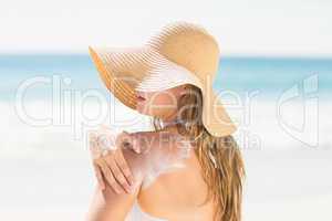 Pretty blonde woman spreading sun tan lotion on her shoulder