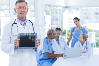 Doctor holding tablet computer while his colleagues works