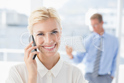 Businesswoman having a phone call with colleague in background