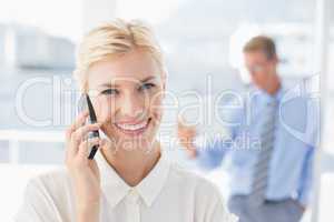 Businesswoman having a phone call with colleague in background