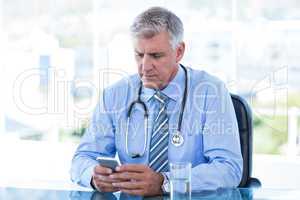 Serious doctor texting with his mobile phone