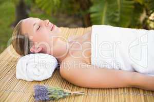 Peaceful blonde lying on bamboo mat with flowers