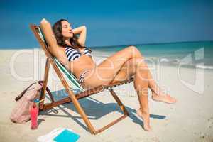 Pretty brunette relaxing on deck chair at the beach