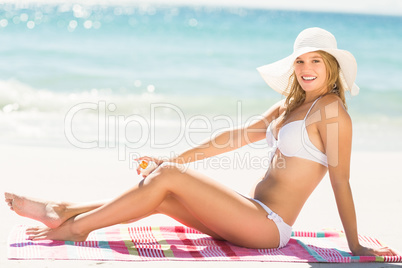 Pretty blonde woman putting sun tan lotion on her leg