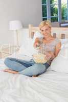 Smiling blonde woman watching TV and eating pop corn