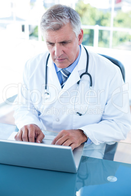 Serious doctor working on laptop at his desk