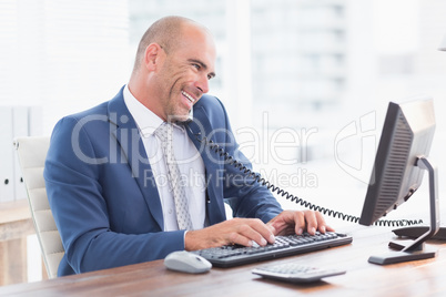 Smiling businessman on the phone and using his computer