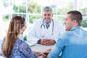Smiling doctor looking at happy couple