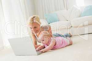 Happy blonde mother with her baby girl using laptop