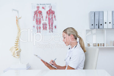Doctor writing on clipboard at her desk