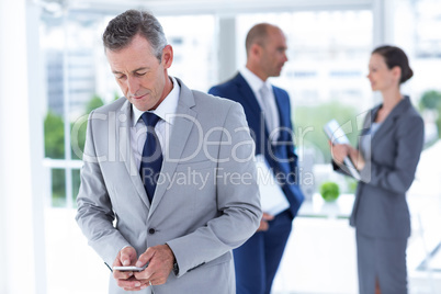 businessman using her phone with two colleague behind him