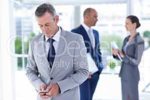 businessman using her phone with two colleague behind him