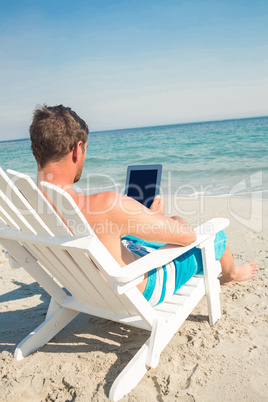 Man using digital tablet on deck chair at the beach