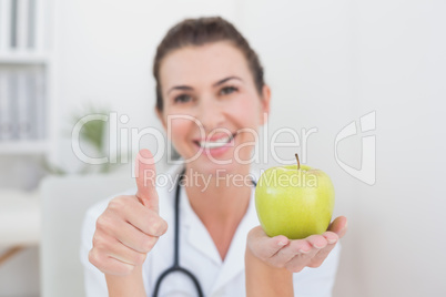 Smiling doctor showing apple with thumbs up