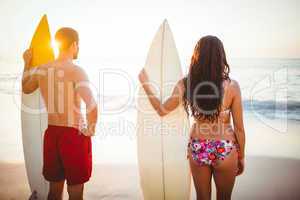 Couple holding surfboards looking at ocean