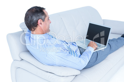 Smiling businessman lying on a sofa holding a laptop