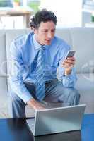 Businessman using laptop and mobile phone on couch