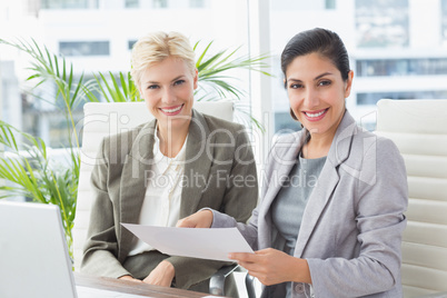 Businesswomen looking at camera and reading files