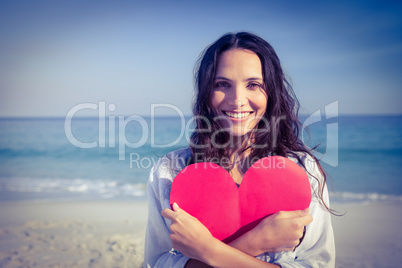 Smiling woman holding heart card at the beach