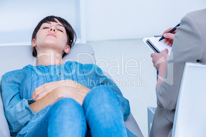 Pensive woman lying on the couch while psychologist writing