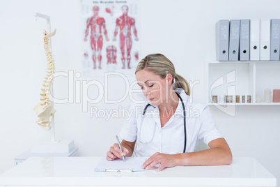 Doctor writing on clipboard at her desk