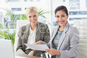 Businesswomen looking at camera and reading files