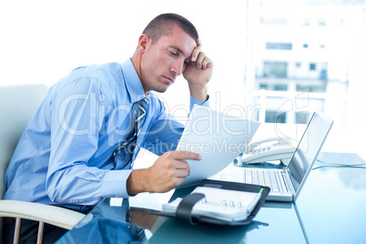 Tired businessman looking at his laptop and his files