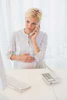 Smiling blonde woman using computer and phoning