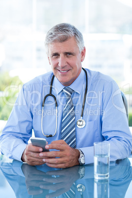 Smiling doctor texting with his mobile phone