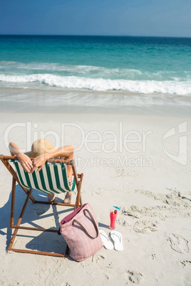 Rear view of pretty brunette relaxing on deck chair at the beach