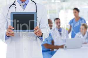 Doctor holding tablet computer while his colleagues works