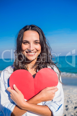 Smiling woman holding heart card at the beach