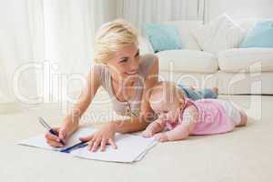 Smiling blonde mother with her baby girl writting on a copybook