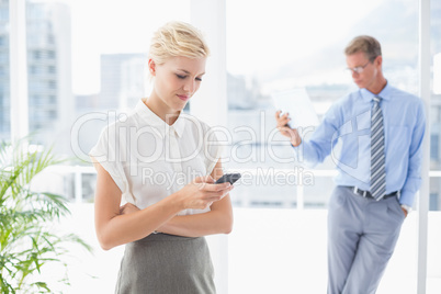 Businesswoman using her smartphone with colleague in background